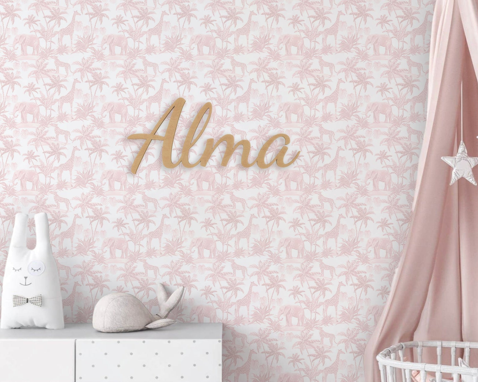Decorative wall with floral pattern, 'Alma' nameplate, and baby items against a pink background