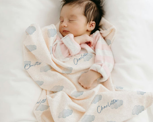 Newborn baby wrapped in a pink blanket with cloud patterns and 'Charlotte' printed on it, lying on a white surface.