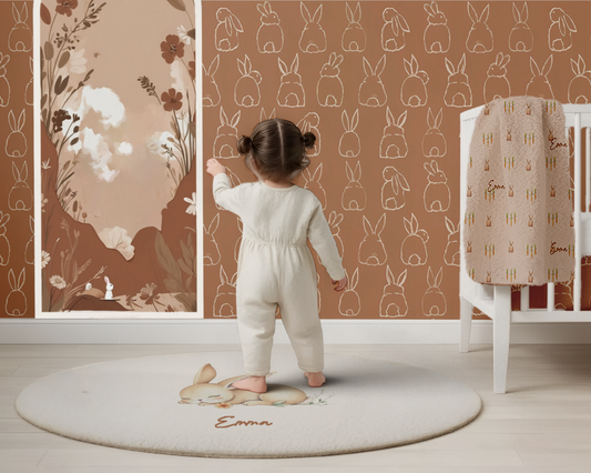 Child in a white outfit standing on a round rug with 'Emma' embroidered, in a room with floral and animal-patterned walls.