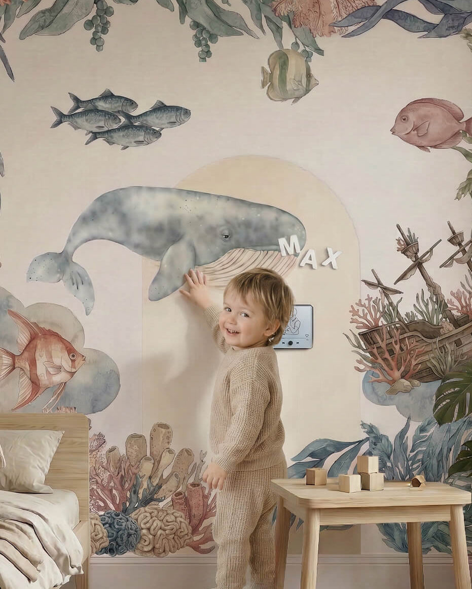 Toddler playing with magnetic alphabet letters on a large watercolor whale wall decal.