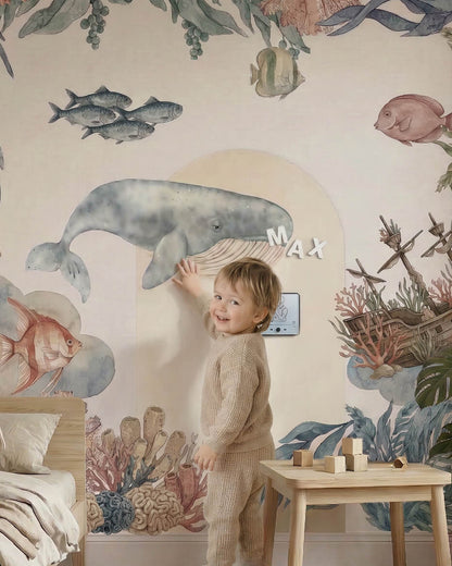 Toddler playing with magnetic alphabet letters on a large watercolor whale wall decal.