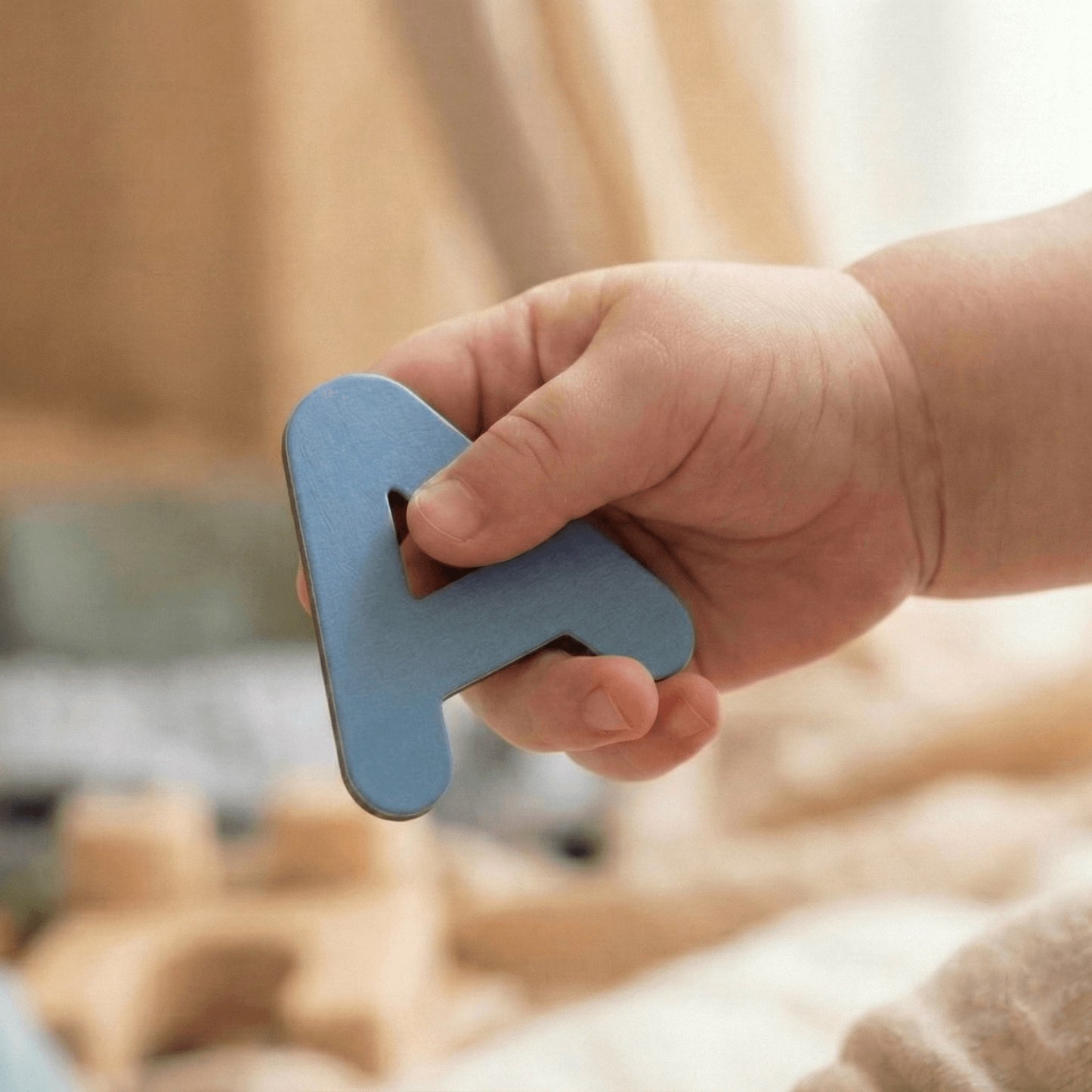 Toddler hand holding blue magnetic wooden letter A for Montessori learning play